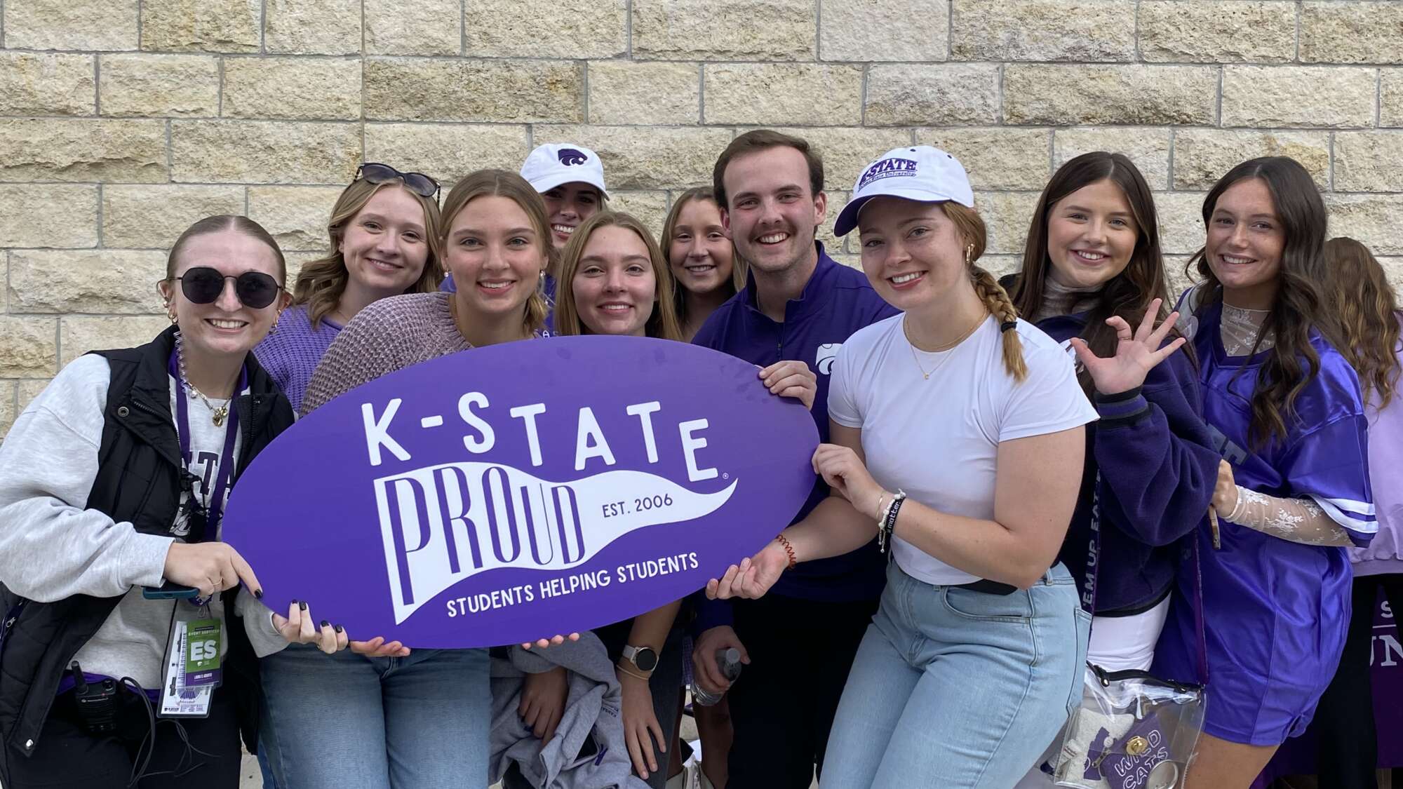 group of students holding an oval shaped sign reading "K-State Proud"