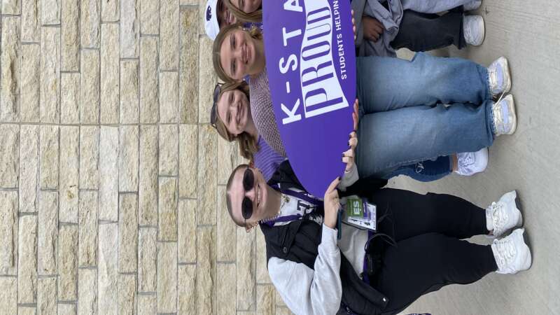 group of students holding an oval shaped sign reading "K-State Proud"