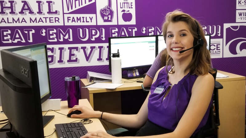 Young woman in purple on the phone in front of a computer.