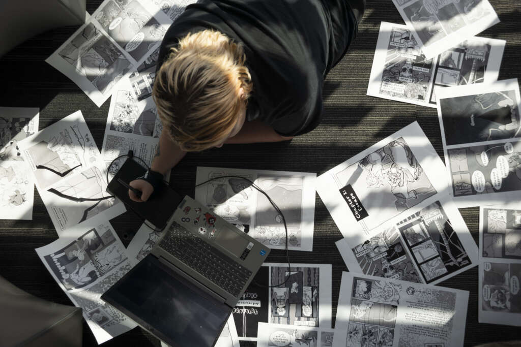 student working on laptop with papers spread around them