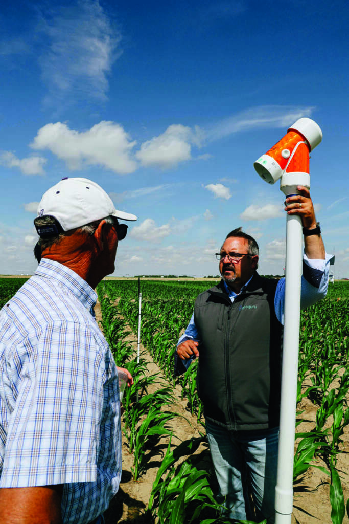 two men talking in a corn field with crop monitoring equipment