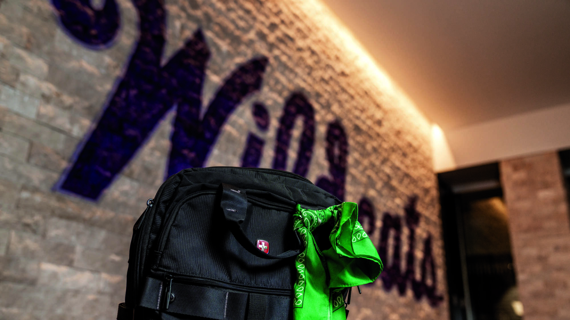 green bandana tied to a blak packpack with the word Wildcats painted on a stone wall in the background