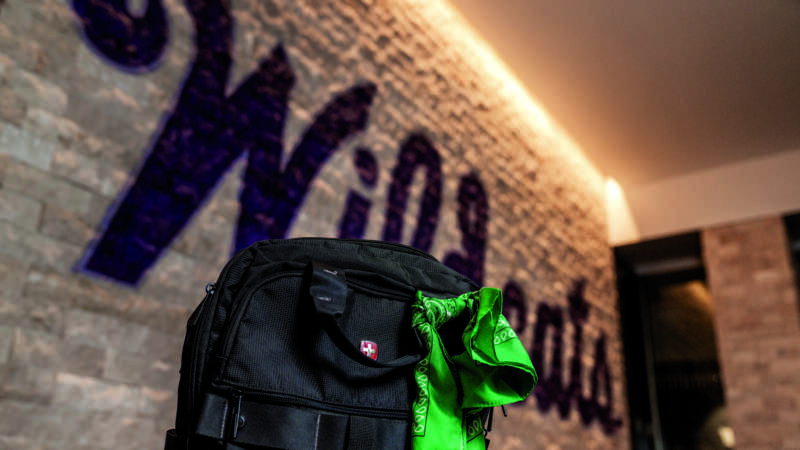 green bandana tied to a blak packpack with the word Wildcats painted on a stone wall in the background