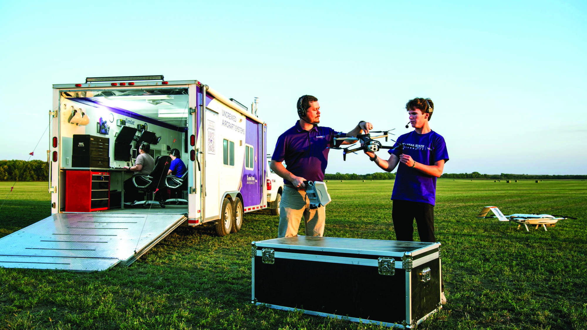 two students holding an unmanned aircraft system in a field near a trailor