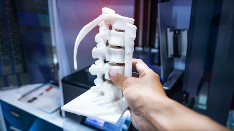 hand with 3d printed human spine in 3d printer