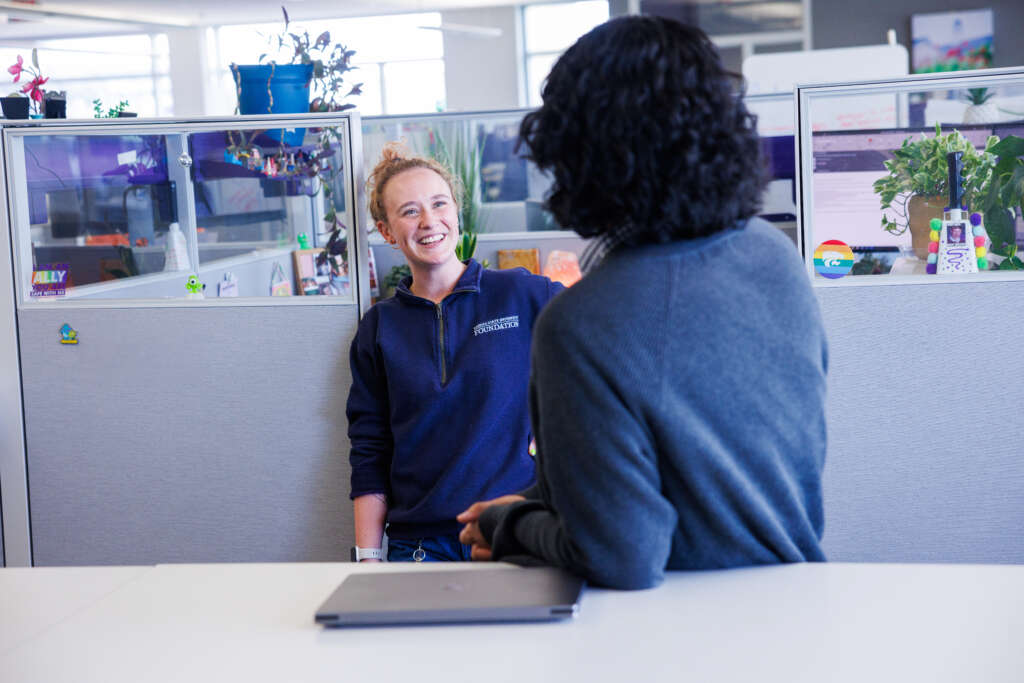two employees talking in front of a cubicle